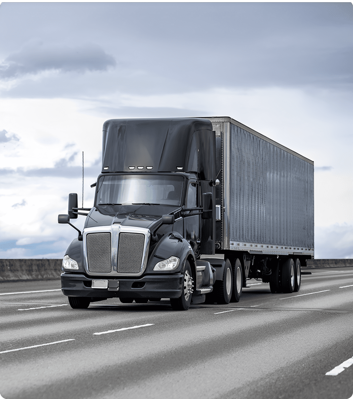 A black semi-truck with a trailer drives on a highway under a cloudy sky.