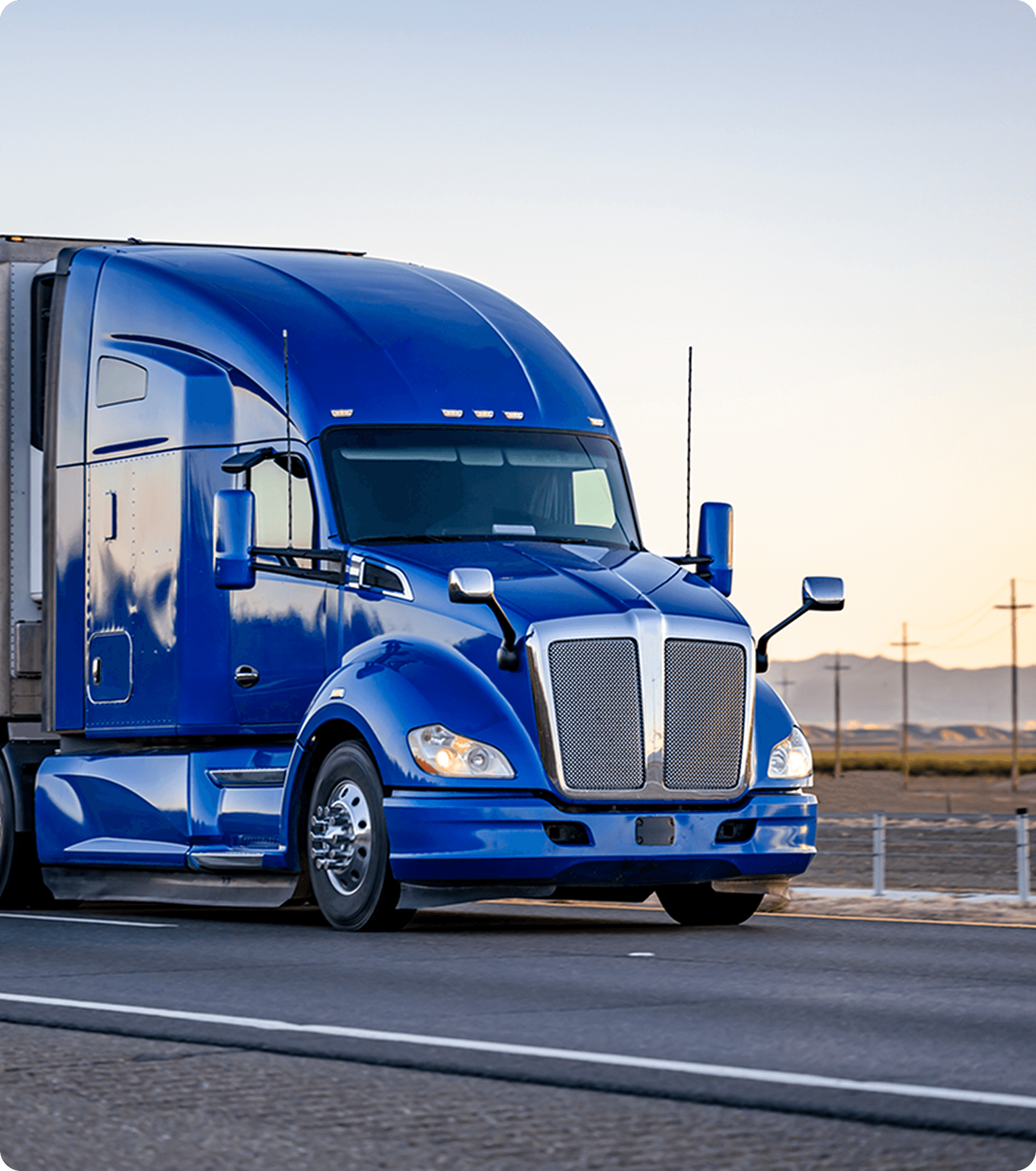 Blue semi-truck driving on a highway with a clear sky and mountains in the background.